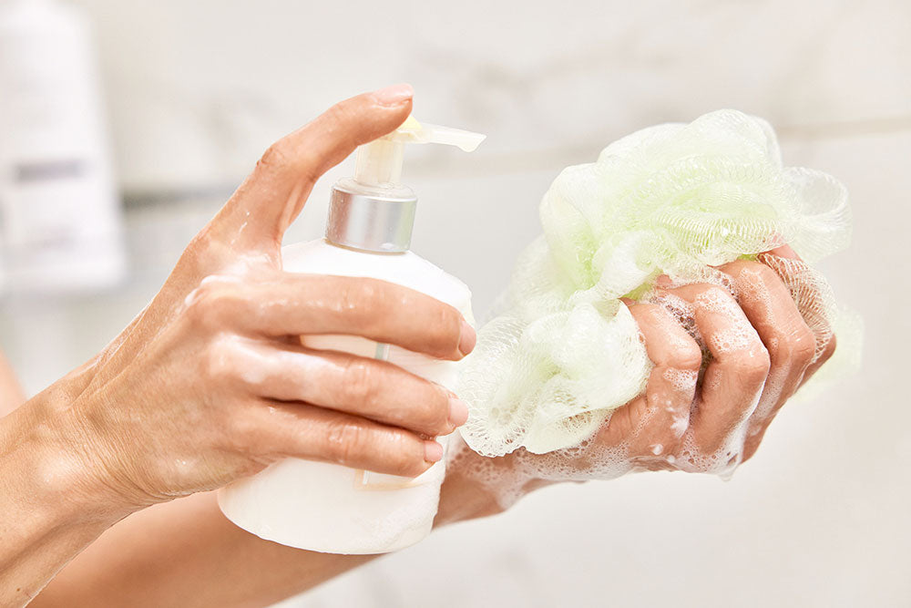 Female hands pouring liquid hand soap from white cosmetic shower gel bottle