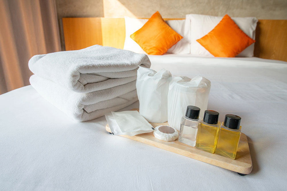 Neatly arranged hotel amenities including towels, shampoo bottles, soap, and packaged items on a bed